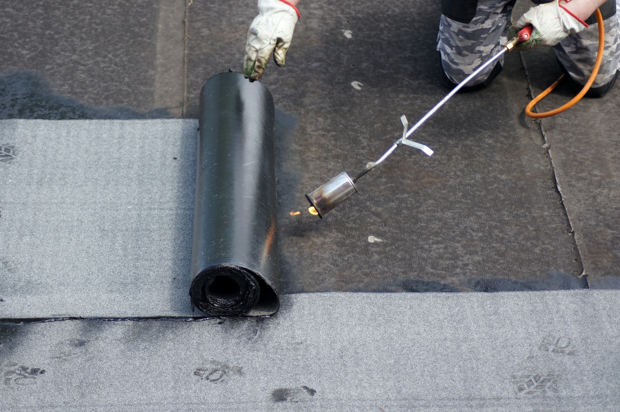 Flat roof installation with propane blowtorch during construction works with roofing felt